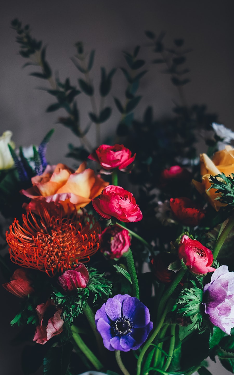Moody arrangement of ranunculus, anemones and an orange pincushion protea