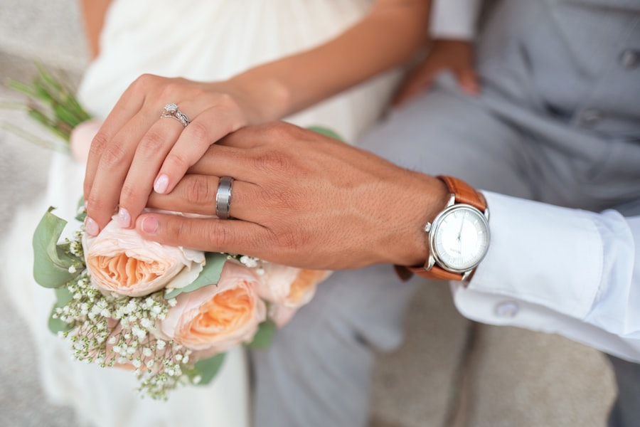 A couple's hands with wedding rings resting on a peach rose bouquet